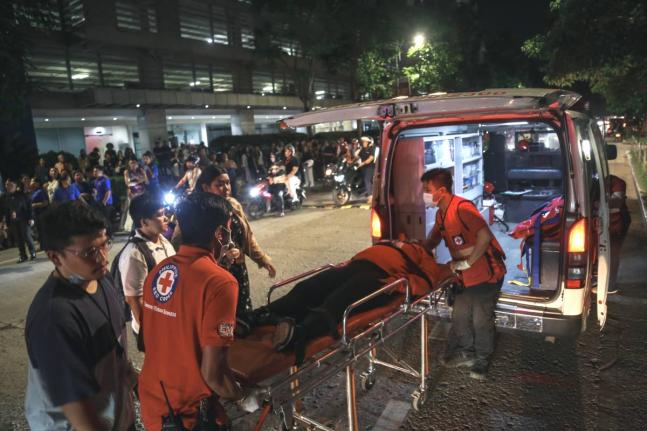 Medical workers load a resident into an ambulance as others stay outside buildings after a strong earthquake struck Cebu city, central Philippines, on Tuesday, September 30, 2025. (AP Photo/Jacqueline Hernandez)