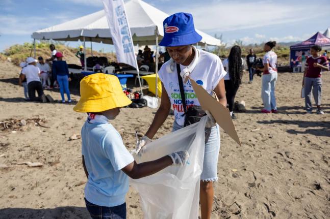 Patrice Smith (right), accounts payables officer at the National Baking Company Limited, holds a bag for her son, Josh-Andrew Brown, to drop waste he collected on Shipwreck Beach in Palisadoes, Kingston, during International Coastal CleanUp Day on Saturday