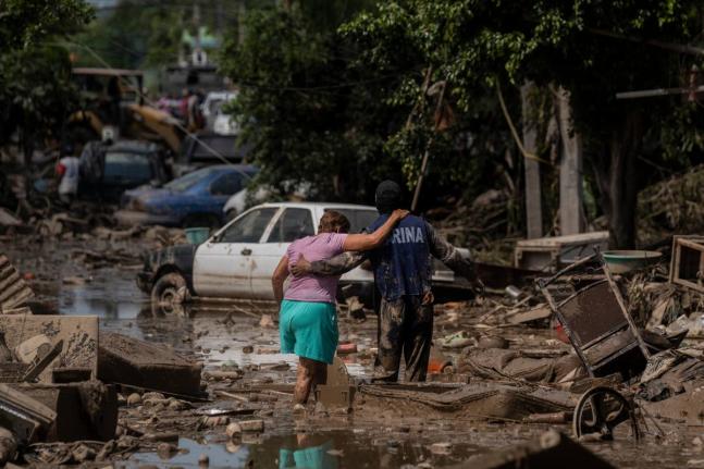 A Marine helps a woman cross a flooded street in Poza Rica, Veracruz state, Mexico, Sunday, October12, 2025. (AP Photo/Felix Marquez)