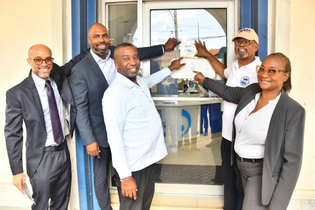 Michael McMorris (second right), chair of the Downtown Kingston Redevelopment Initiative Committee, affixes the decal on the door of Imperial Optical Broadbent on Duke Street. Sharing in the moment on Wednesday are (from left) Jonathan Swire, second vice-p