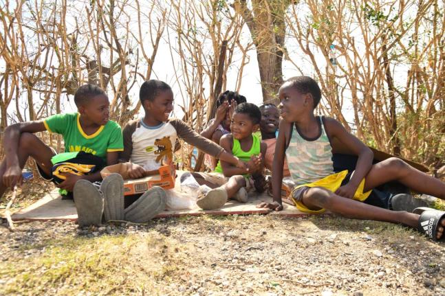 Children sit by the roadside, smiling amid the devastation of their community in Oxford, St Elizabeth, after Hurricane Melissa.