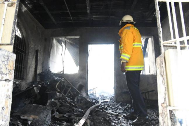 A firefighter surveys the charred remnants of Ray Moore’s home on Mountain View Avenue in St Andrew yesterday. Several burnt speaker parts can be seen scattered about.