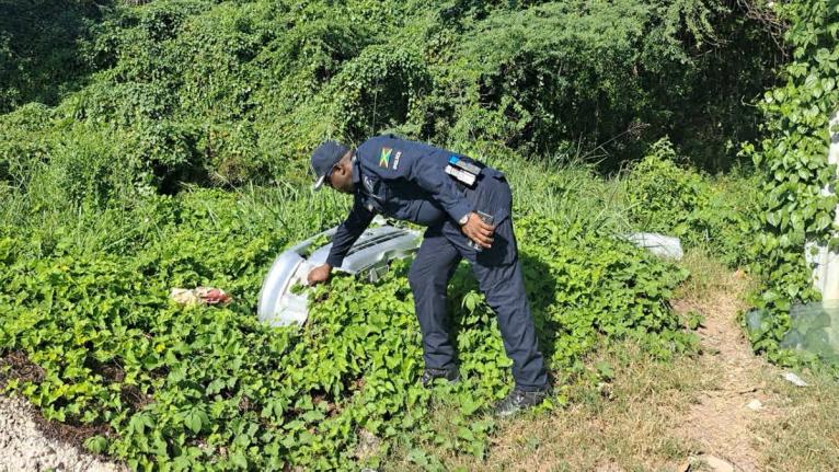 Senior Superintendent Hopeton Nicholson, head of the St Catherine North Police, retrieves a motor-vehicle bumper from bushes during a raid at a premises off St John's Road in Spanish Town on December 12, 2025. 