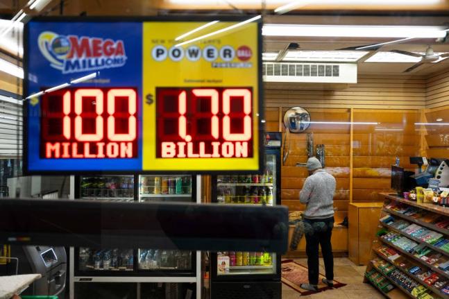 A convenience store employee prays while Jackpot payouts for Powerball and Mega Millions are displayed outside the store, Tuesday, December 23, 2025, in New York. (AP Photo/Yuki Iwamura)