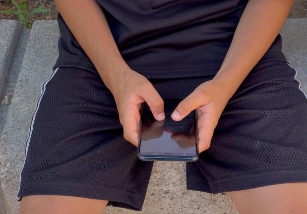 A 12-year-old boy plays with his personal phone outside school.