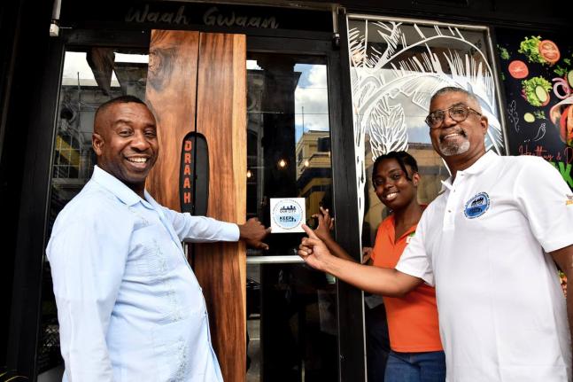 Sherina Whyte (centre) , co-founder of Waah Gwaan Café, affixes the ‘Keep It Clean’ sticker decal on the door of her business place. Sharing in the moment are Councillor Andrew Swaby (left), mayor of Kingston and chairman of the Kingston and St Andrew