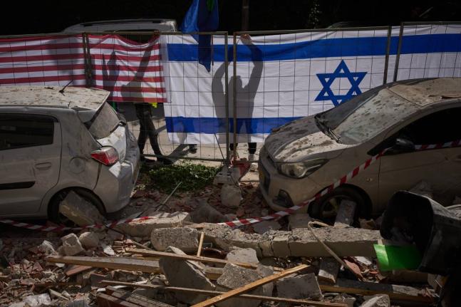 Israeli authorities hang Israeli and United States flags at the site struck by an Iranian missile that killed two people, in Ramat Gan, Israel on March 18, 2026. (AP Photo/Oded Balilty)