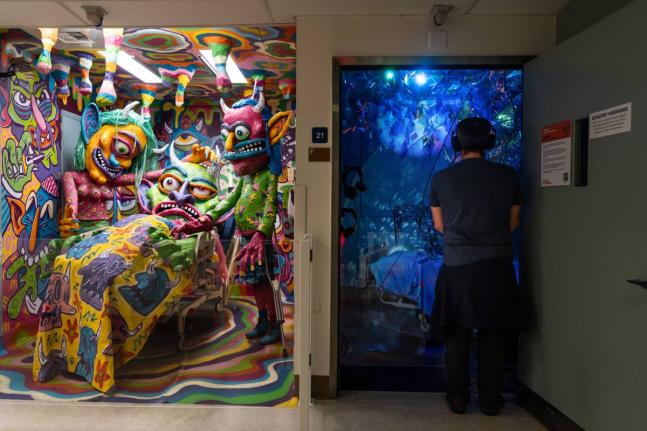 A visitor views an installation by Margüi while standing beside an installation by Guy “Dioz” Bloom during the “Hospital of Emotions” exhibition inside a former hospital building in Los Angeles.