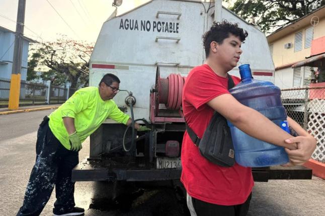 Bryan Pérez hauls a five-gallon water jug to his apartment in the Villa Kennedy public housing complex in San Juan, Puerto Rico, June 10, 2026.