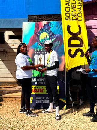 Tashalee Billings, committee member of Wake-Fit 10K Run/Walk, presents winner of the 10K Run in the 17 and over category Jaheim Morrison with his trophy, following the second staging of Wake-Fit 10K Run/Walk in Wakefield, Trelawny, on Saturday, August 1.