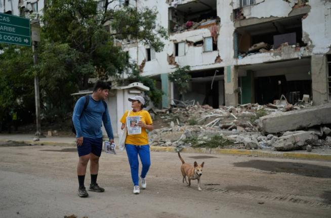 Pedro Gomez, left, walks through La Guaira, Venezuela, with a friend, asking people if they have seen his cousin, Andres Molina, who has been missing since the earthquakes, Saturday, August 22, 2026. (AP Photo/Ariana Cubillos) 