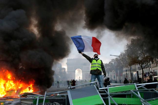 A demonstrator wearing a yellow vest waves the French flag on top of a burning barricade on the Champs-Elysees avenue with the Arc de Triomphe in background in Paris, on Saturday, Nov. 24, 2018, during a demonstration against the rising fuel taxes. 
