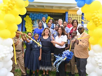 American Friends of Jamaica President Wendy Hart (fourth left) cuts the ribbon officially handing over the rebuilt Cove Primary in Hanover, along with Heidi Clarke of Sandals Foundation (second right) and  students and members of management of the school l