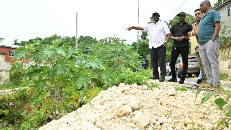 Minister of Local Government and Community Development, Desmond McKenzie (left), assesses the condition of the main road in Top Burnt Ground, St Elizabeth, on Friday (October 9), where plans are being considered for the construction of a retaining wall to 