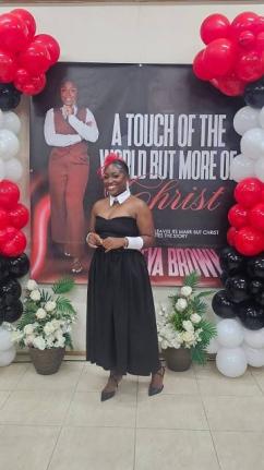 Tameya Brown, Salt Spring author, poses in front of a giant backdrop featuring the cover of her debut book, ‘A Touch of the World but More of Christ’.